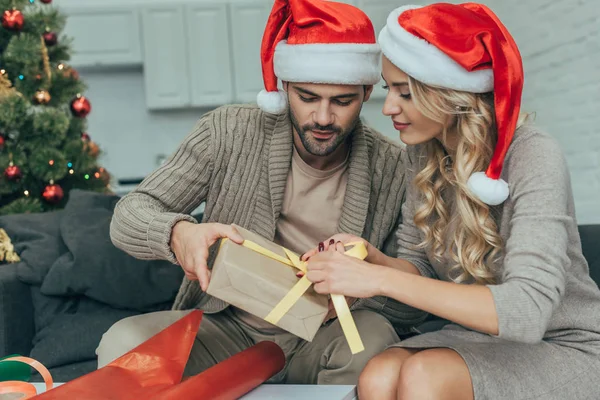 Focused Young Couple Santa Hats Decorating Christmas Gift Together Home — Stock Photo, Image