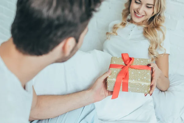 Recortado Disparo Hombre Joven Presentando Regalo Novia Cama Casa — Foto de Stock