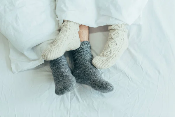 cropped shot of couple in woolen socks lying in bed together at home