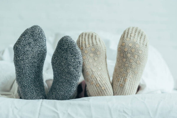 cropped shot of couple in warm woolen socks lying in bed together at home