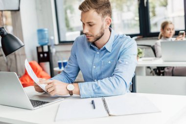 kağıtları tutarak ve dizüstü Office ile çalışan genç işadamı