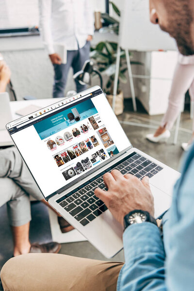 cropped shot of young businessman using laptop with amazon website on screen  