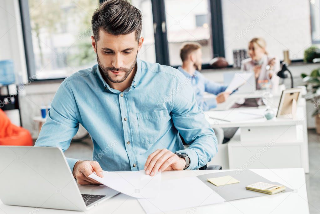 professional young businessman working with papers and using laptop at workplace