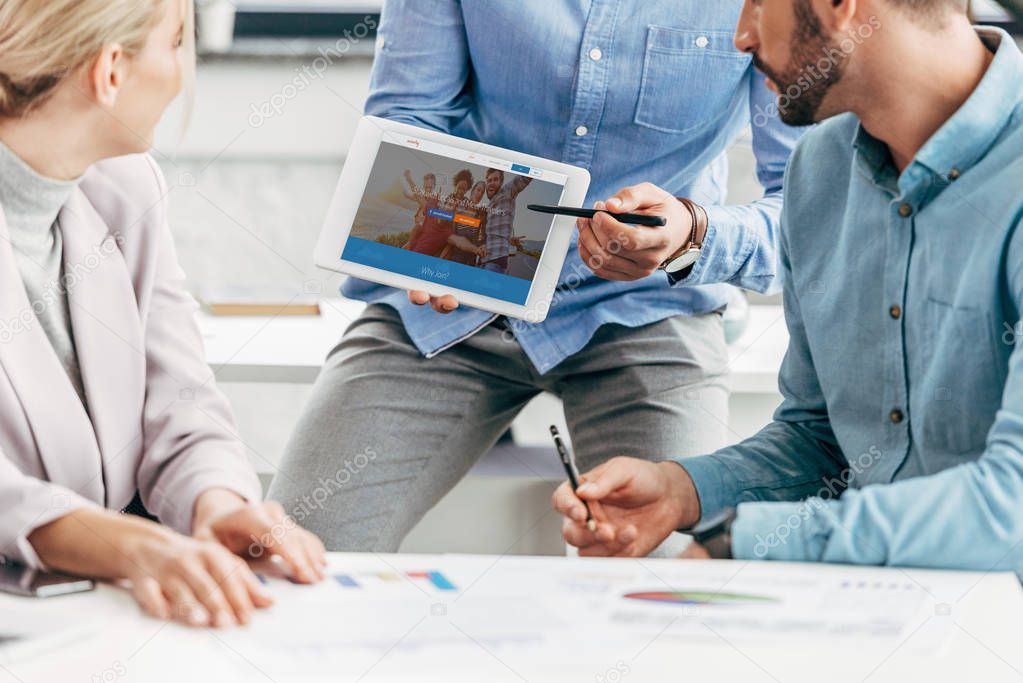 Cropped shot of businessman showing digital tablet with couchsurfing website to colleagues at workplace
