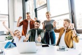 Skupina mladých úspěšných podnikatelů slaví vítězství a objevovat palce v kanceláři a při pohledu na fotoaparát