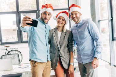 mutlu genç selfie ile smartphone içinde göreve Noel Baba şapkaları takımda başlatmak