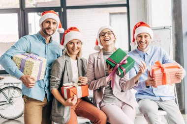 mutlu arkadaşları hediye tutarak ve kamera Office gülümseyen santa şapkalar