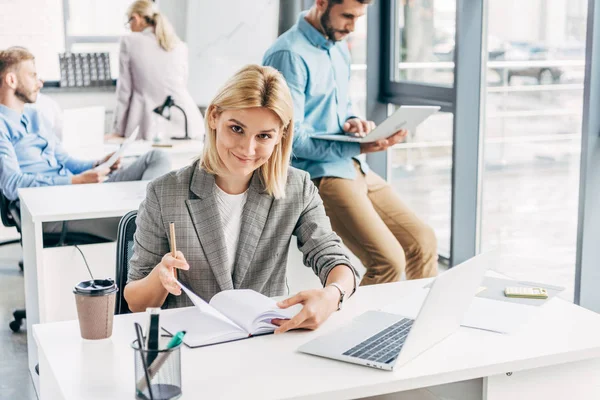 Hermosa Joven Empresaria Sonriendo Cámara Mientras Sus Colegas Trabajan Detrás — Foto de Stock