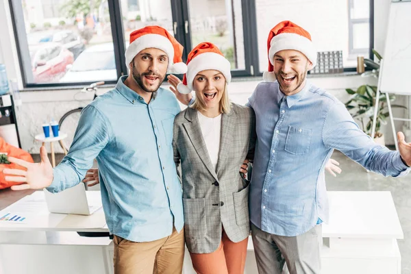 愉快的年轻的商业团队在圣诞老人的帽子微笑在办公室的相机 — 图库照片