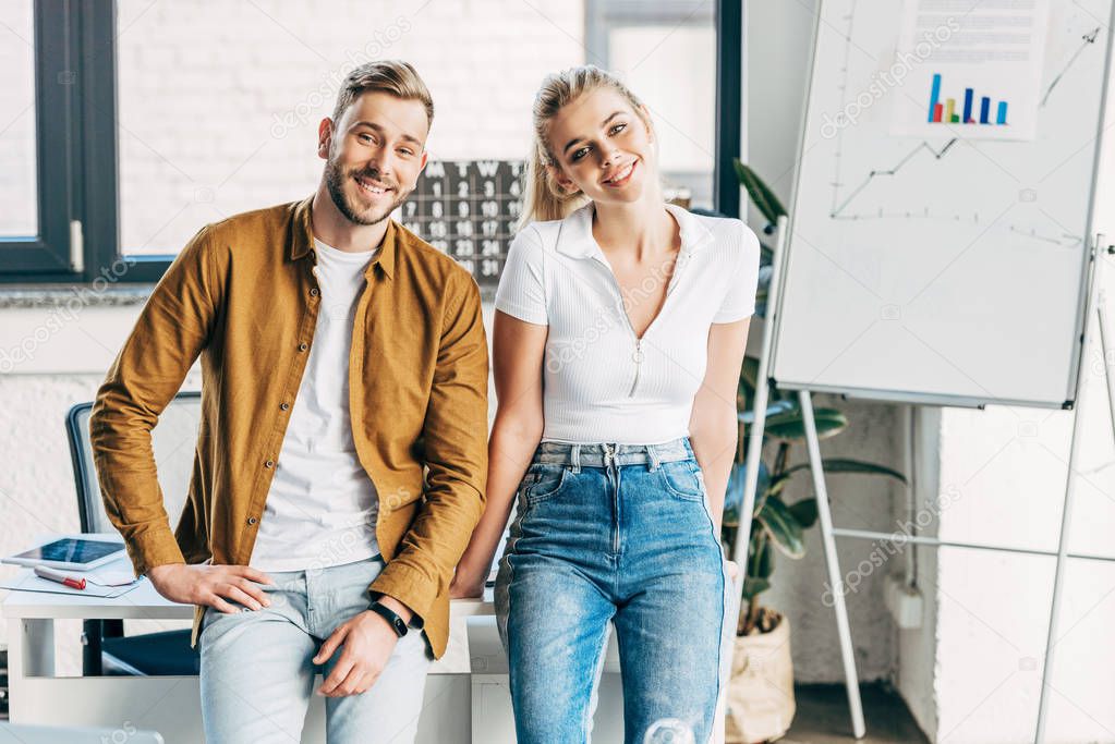 young casual man and woman sitting on tablet at office and looking at camera