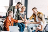 Skupina happy mladých podnikatelů dělat tým gesto, zatímco spolupracují na startu v kanceláři