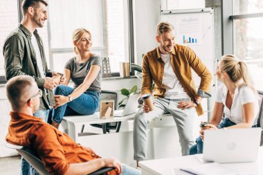 group of young entrepreneurs chatting while working on startup together at office clipart