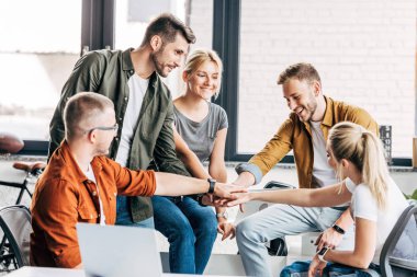 group of happy young entrepreneurs making team gesture while working on startup together at office clipart