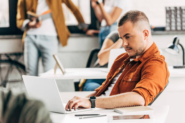 young man working with laptop at open space office with colleagues on background