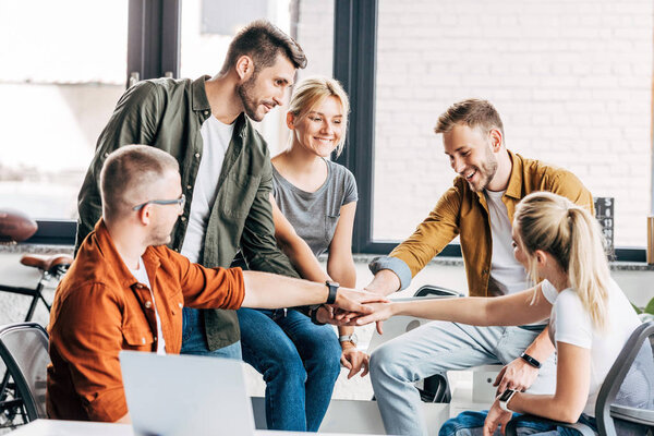 group of happy young entrepreneurs making team gesture while working on startup together at office