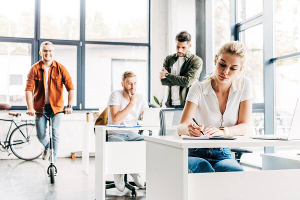 group of young entrepreneurs working on startup together at modern open space office while man riding scooter on background