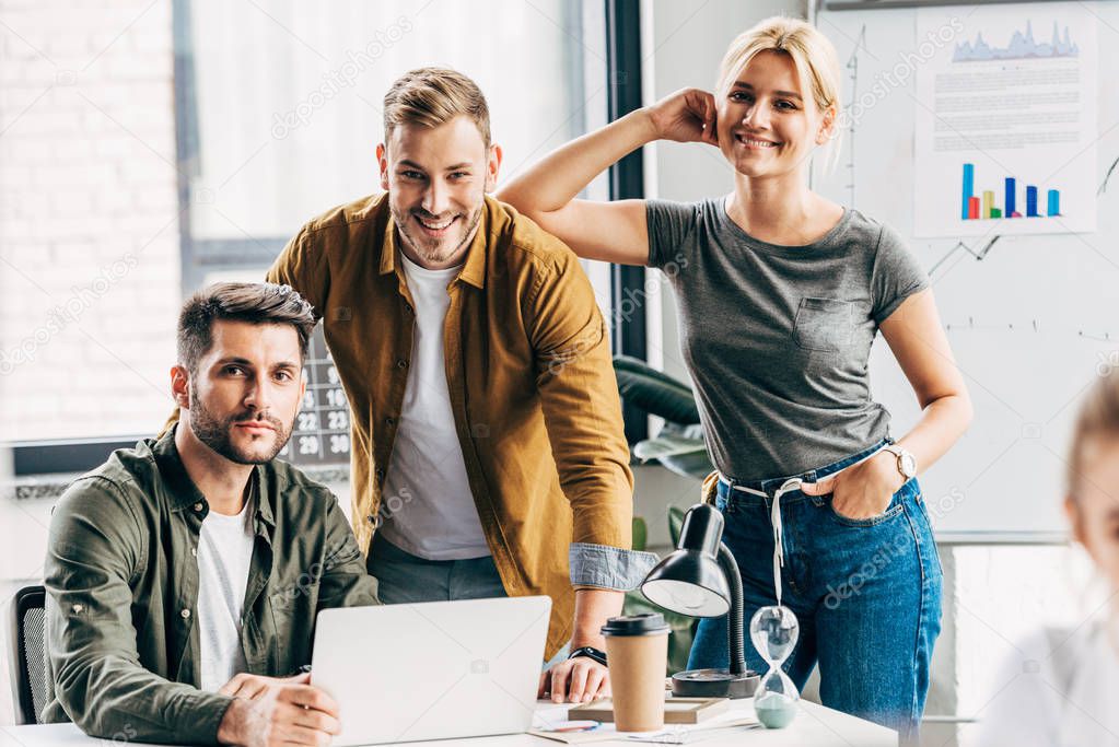 group of young managers working with laptop together at office and looking at camera