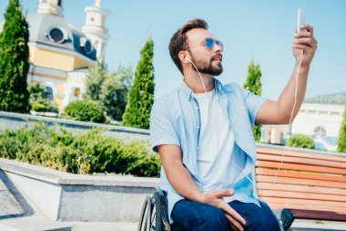 selfie ile smartphone alarak ve sokakta müzik dinlemek tekerlekli sandalyede yakışıklı adam