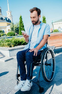 smartphone kullanarak ve sokakta müzik dinlemek tekerlekli sandalyede yakışıklı adam