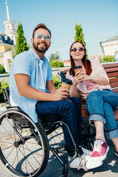 通りに紙コップでコーヒーを飲みながら車椅子とガール フレンドのハンサムな彼氏を笑ってください — ストック写真