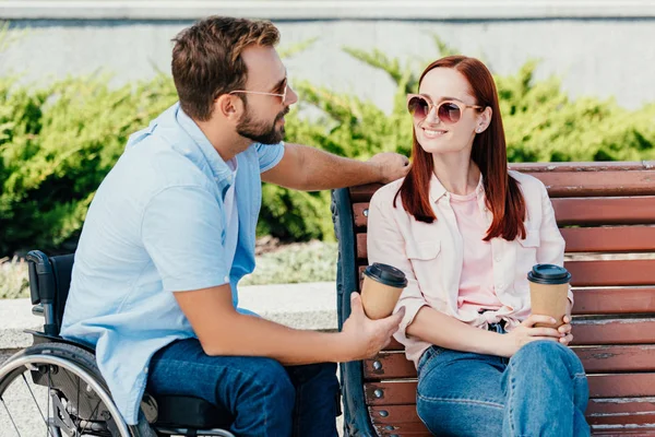 handsome boyfriend in wheelchair and girlfriend with coffee to go looking at each other outside