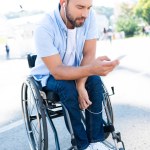 Pohledný muž vozíku poslechu hudby s smartphone na ulici