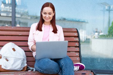 şehirde bankta dizüstü kullanarak çekici gülümseyen Dişileştirilmiş serbest meslek