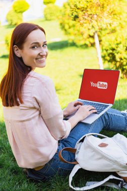 gülümseyen çekici kadın Parkı ve kameraya bakarak yüklü youtube sayfası ile dizüstü bilgisayar kullanarak