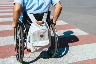 cropped image of disabled man in wheelchair with bag riding on crosswalk clipart