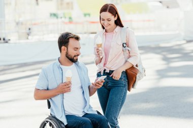 Tekerlekli sandalye ve kız sokakta smartphone kullanarak dondurma ile yakışıklı erkek