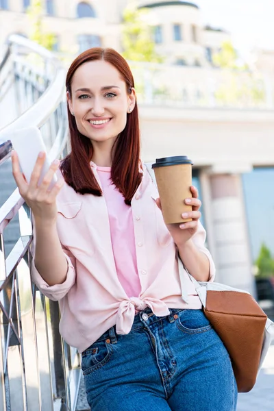 Attraktiva Redhair Kvinna Rosa Skjorta Hålla Smartphone Med Disponibla Kaffekopp — Gratis stockfoto