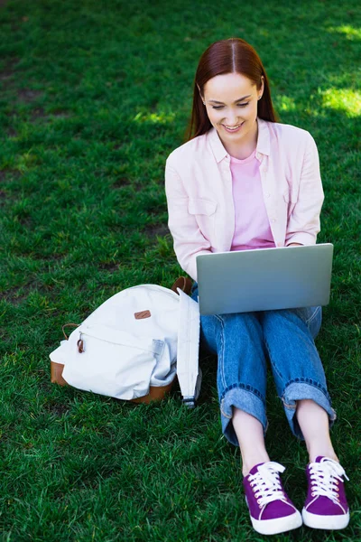 有吸引力的自由职业者使用笔记本电脑和坐在绿色草地在公园 — 免费的图库照片