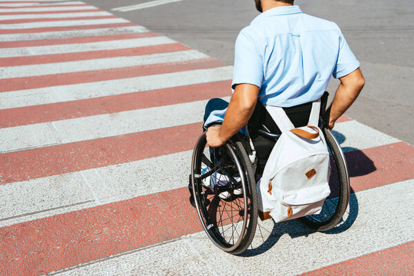 обрезанное изображение человека в инвалидной коляске на переходе по улице

