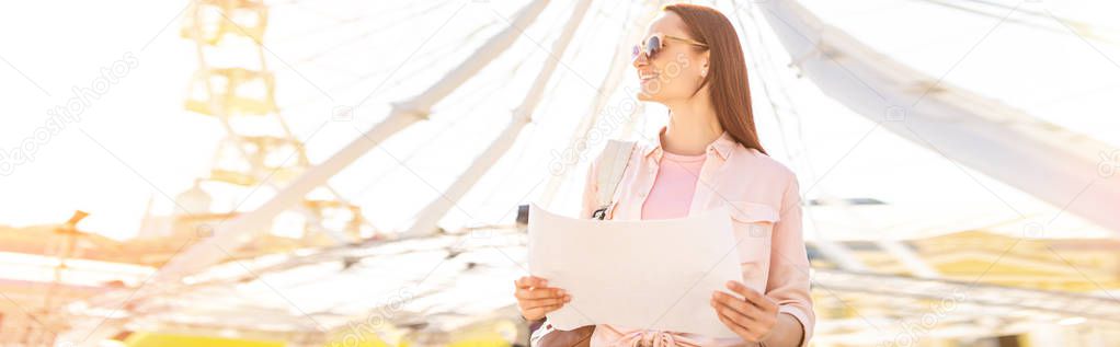 panoramic view of attractive tourist in sunglasses standing with map near observation wheel