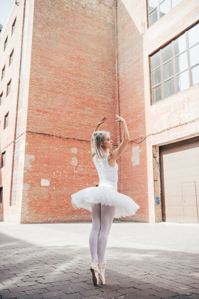 back view of young ballerina dancing on urban city street