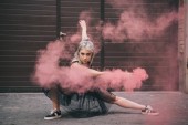 krásná dívka tančí v růžové kouře a při pohledu na fotoaparát na ulici 