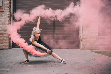 Genç kadın pembe duman içinde kentsel sokakta dans 