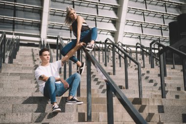 merdiven ve korkuluklar üzerinde oturan sırt çantaları ile şık sportif genç çift