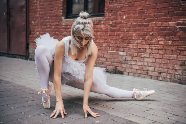 attractive young ballerina stretching on street