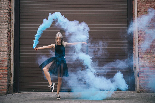 girl dancing in blue smoke and looking at camera on urban city street
