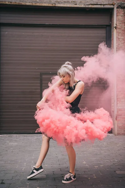 美丽的年轻女舞蹈家跳舞在粉红色烟雾在街道上 — 图库照片