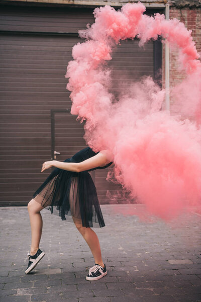 flexible young woman dancing in pink smoke on urban street  