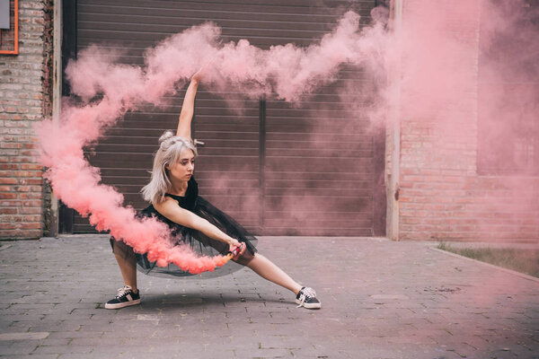 young woman dancing in pink smoke on urban street 