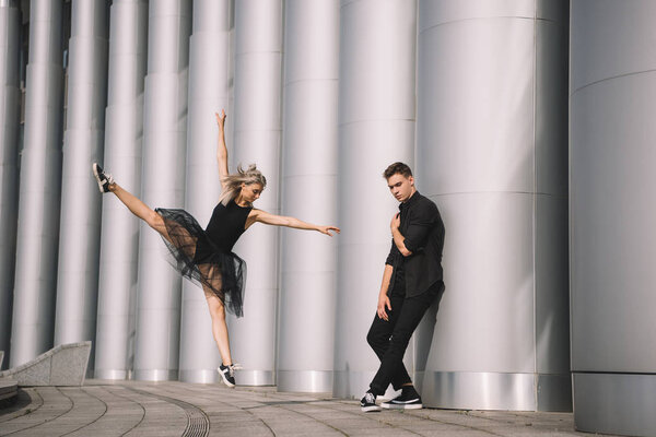 молодая пара танцовщиц в черной одежде танцует возле колонн
   