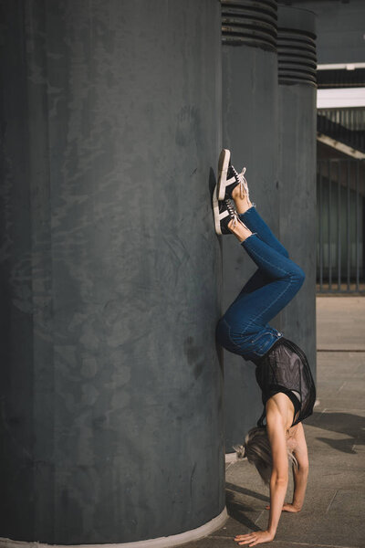 beautiful young woman performing handstand near black column