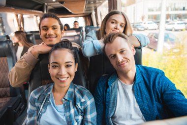 portrait of happy multicultural friends looking at camera during trip on travel bus  clipart
