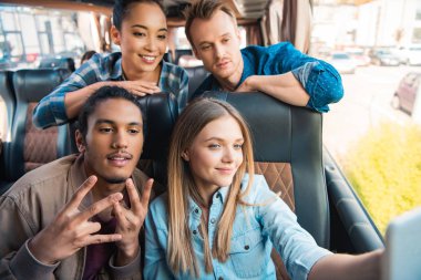happy multiethnic friends taking selfie on smartphone during trip on travel bus clipart