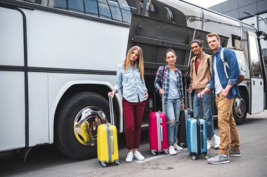 multicultural friends with travels bags posing near travel bus at street
