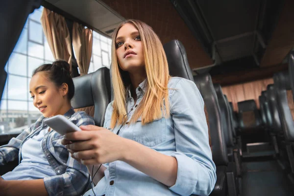 妇女的选择性重点与智能手机 而她的亚洲女性朋友坐在旅行巴士旅行附近 — 图库照片