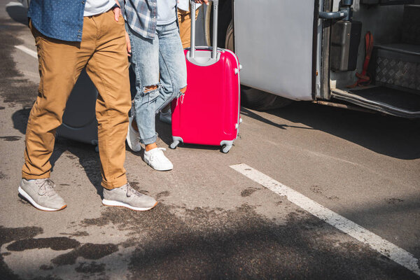 cropped image of friends with wheeled bags walking near travel bus at street 